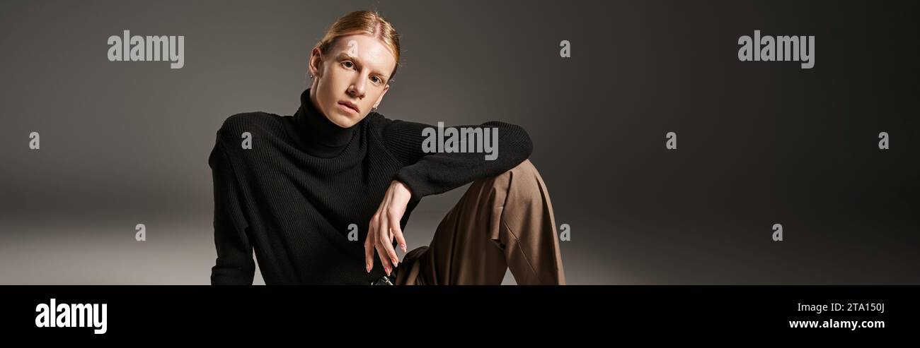 Attraktive, nicht binäre Person mit schwarzem Rollkragen, die auf dem Boden sitzt und auf die Kamera und das Banner blickt Stockfoto