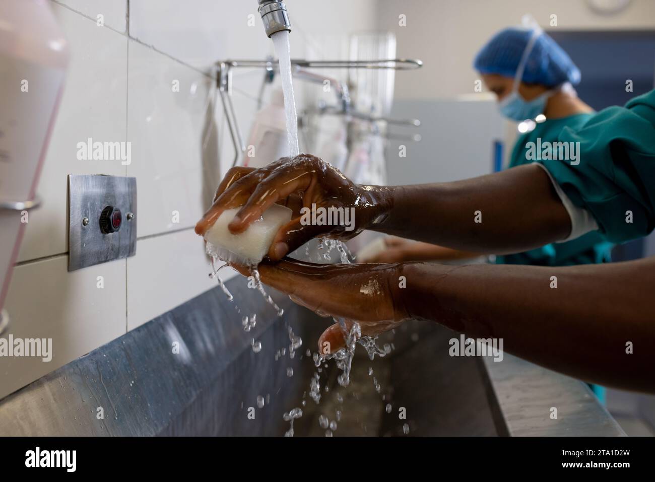 Hände diverser männlicher und weiblicher Chirurgen mit Gesichtsmasken, die Hände im Krankenhaus waschen Stockfoto