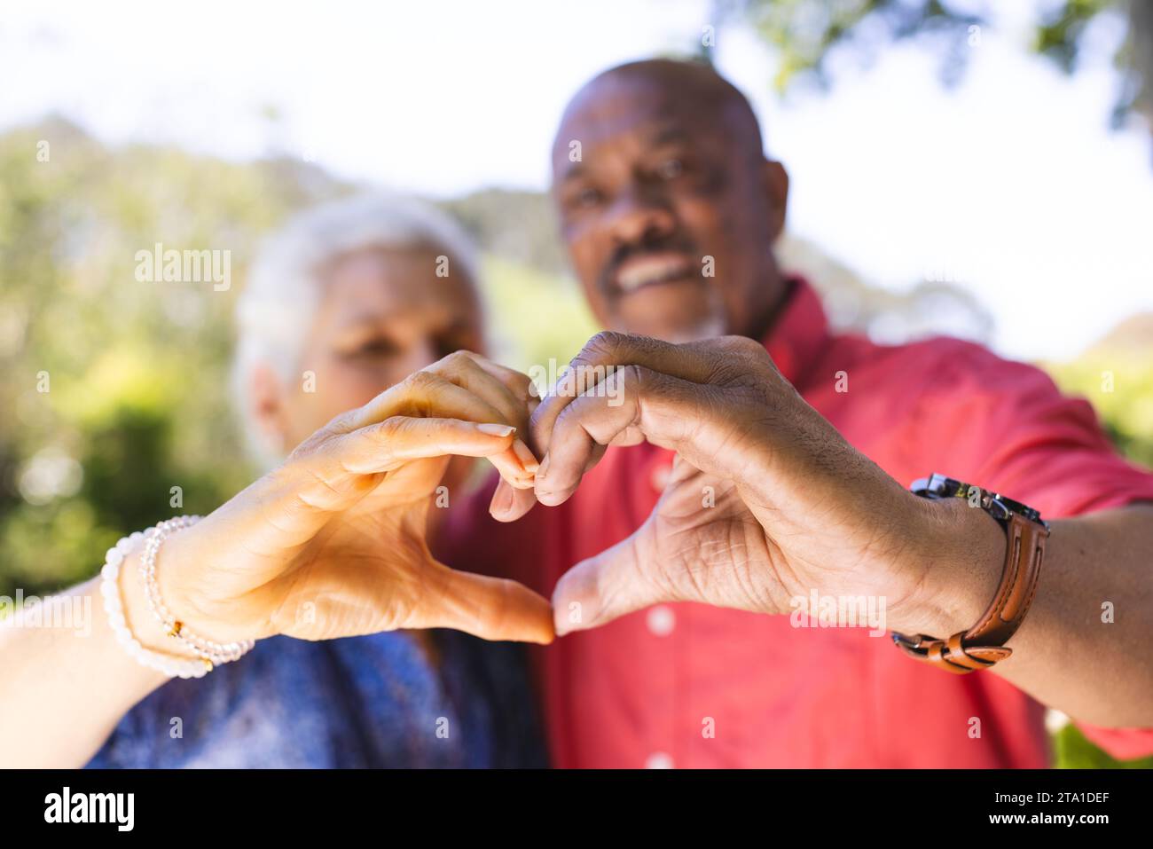Hände eines glücklichen, vielseitigen Seniorenpaares mit Herzform im sonnigen Garten. Lebensstil, Ruhestand, Seniorenleben, Natur, Zweisamkeit und Domesti Stockfoto