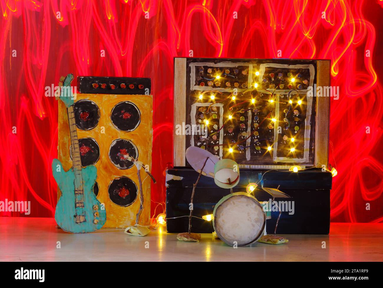 Grungy Pappmodelle von Synthesizer, Schlagzeug, Gitarre, Verstärker und Mikrofon auf der Bühne mit wilden Lichtspuren, Musik, Performance, Instrumentenkonzept, Stockfoto