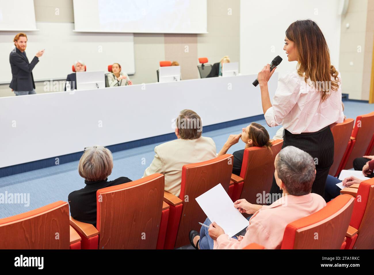 Frau, die im Publikum steht und mit dem Sprecher während der Geschäftskonferenz im Auditorium diskutiert Stockfoto