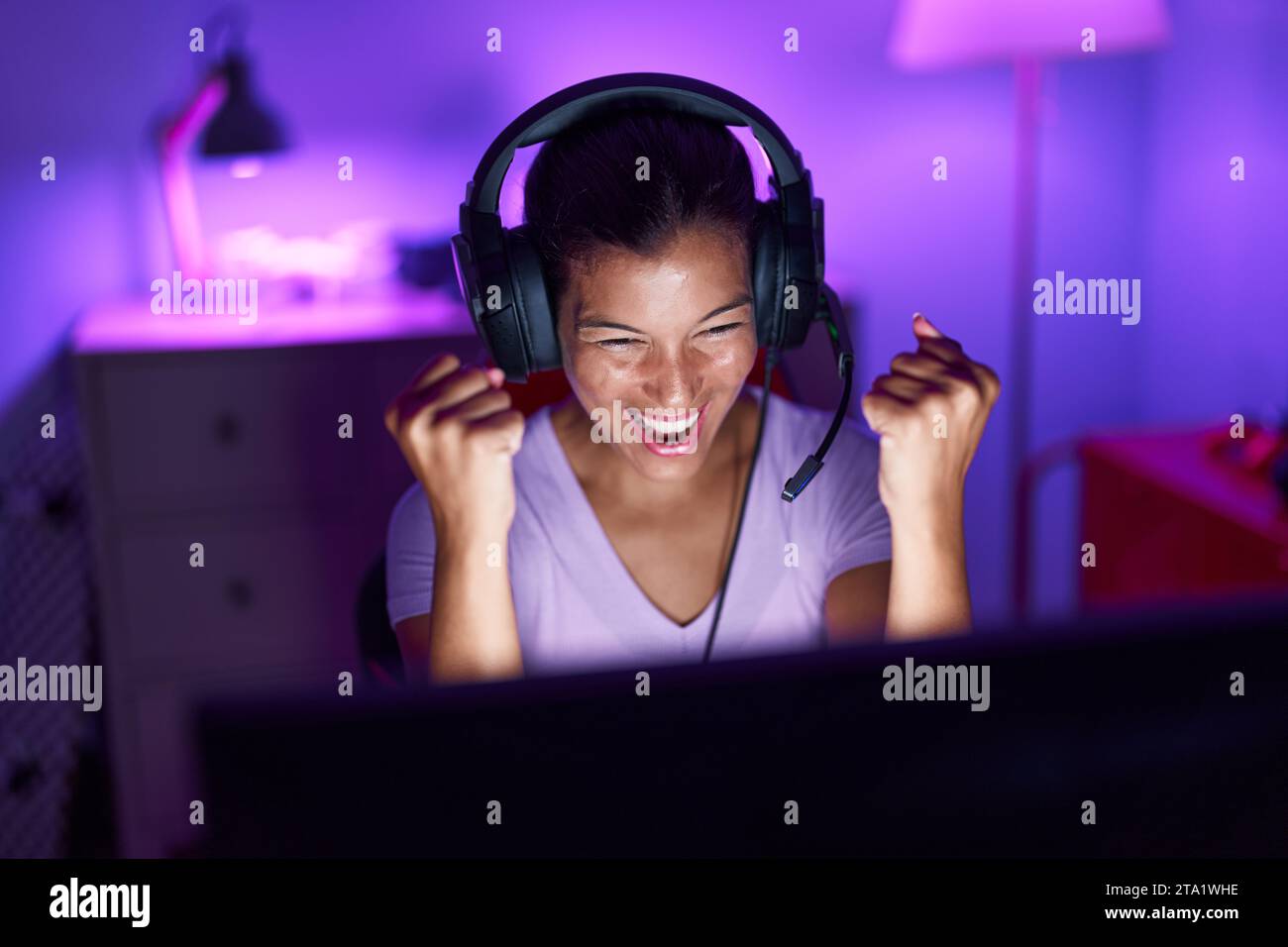Junge schöne hispanische Frau streamer spielen Videospiel mit Sieger Ausdruck in Gaming-Raum Stockfoto