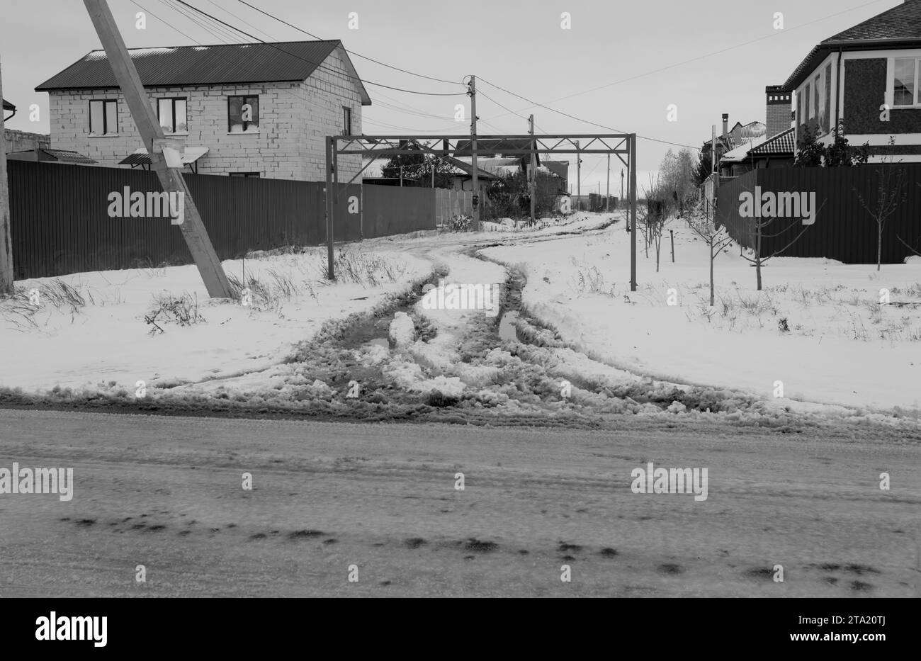 Verschneite Straße auf dem Land. Driftet auf einer unbepflügten, schneebedeckten Landstraße durch Cottage Community. Autospuren im Winter. Das Konzept des gefährlichen Drivi Stockfoto