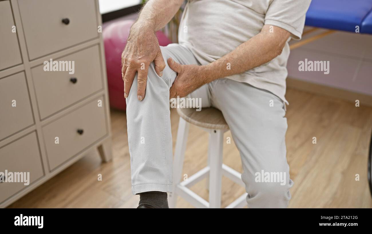 Seniorenhände berühren das Knie bei Schmerzen, leiden in der Reha-Klinik während der physiotherapeutischen Behandlung Stockfoto