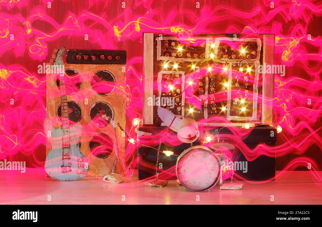 Grungy Pappmodelle von Synthesizer, Schlagzeug, Gitarre, Verstärker und Mikrofon auf der Bühne mit wilden Lichtspuren, Musik, Performance, Instrumentenkonzept, Stockfoto
