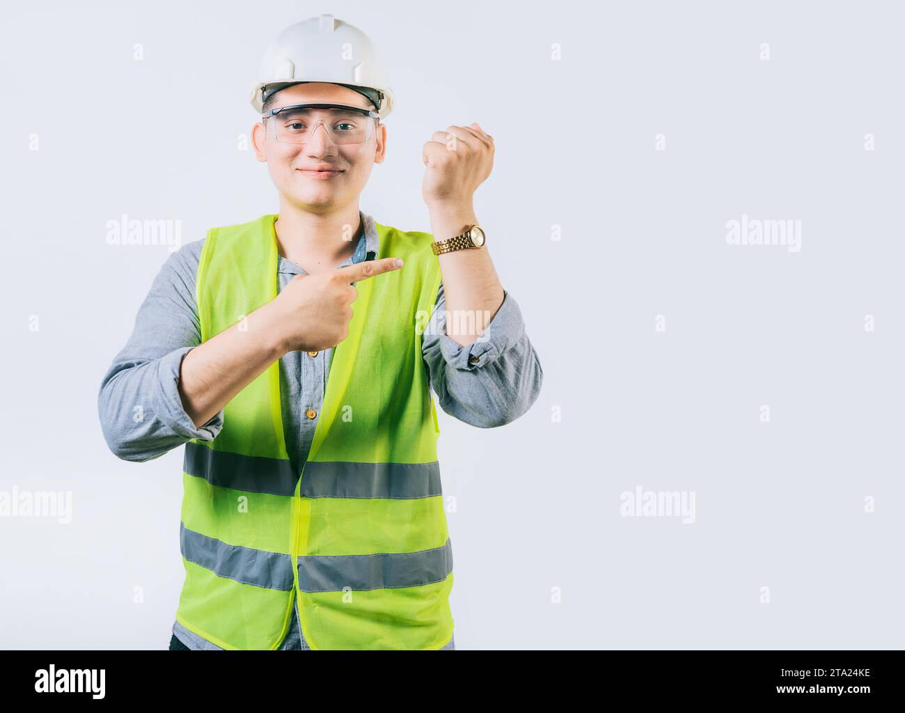 Lächelnder Ingenieur, der auf seine Armbanduhr zeigt. Junger Ingenieur zeigt und zeigt seine Armbanduhr Stockfoto