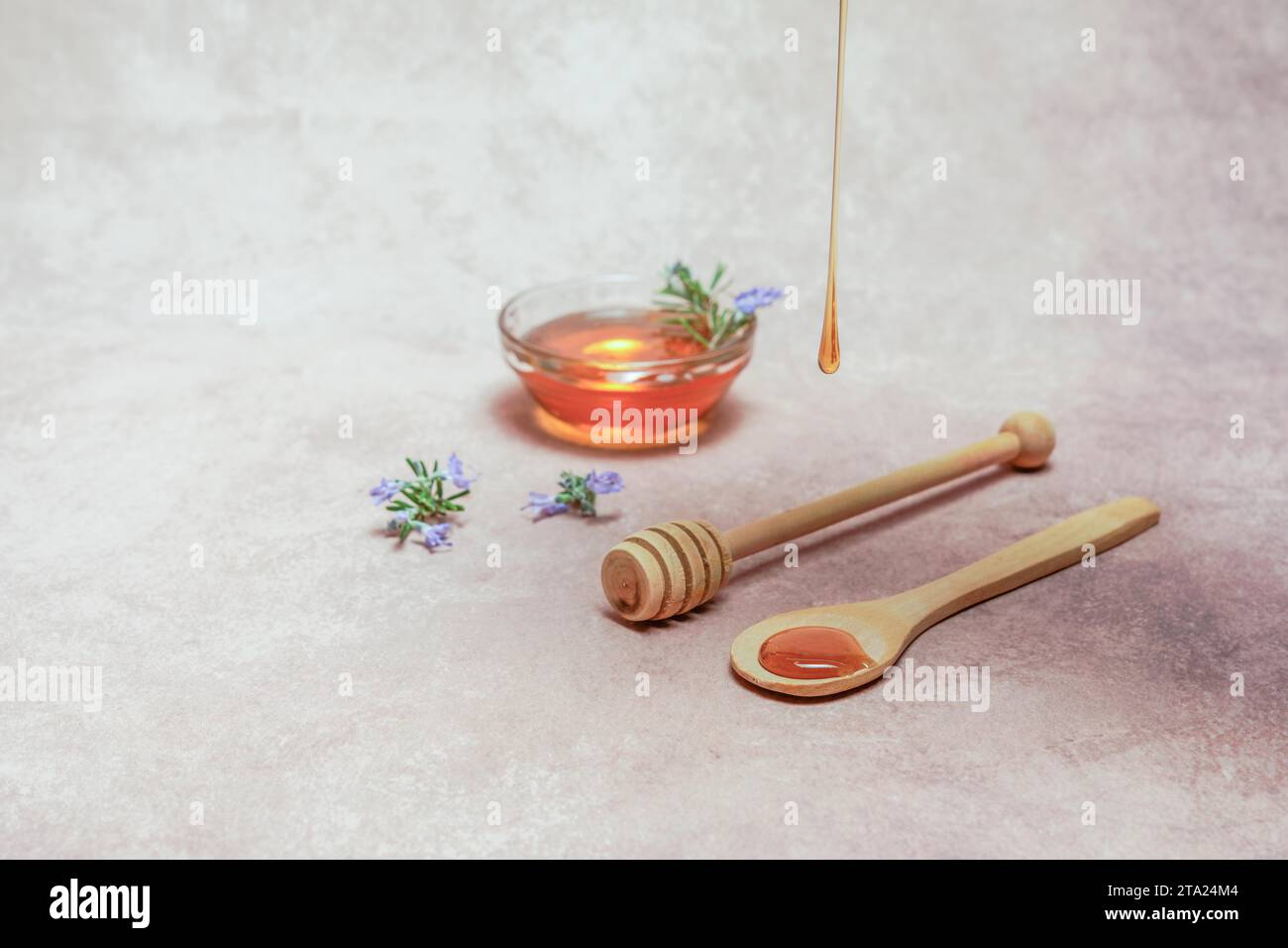 Natürlicher Honig tropft auf einem Holzlöffel mit Rosmarinblütenzweigen und einer Schüssel mit Honig Stockfoto