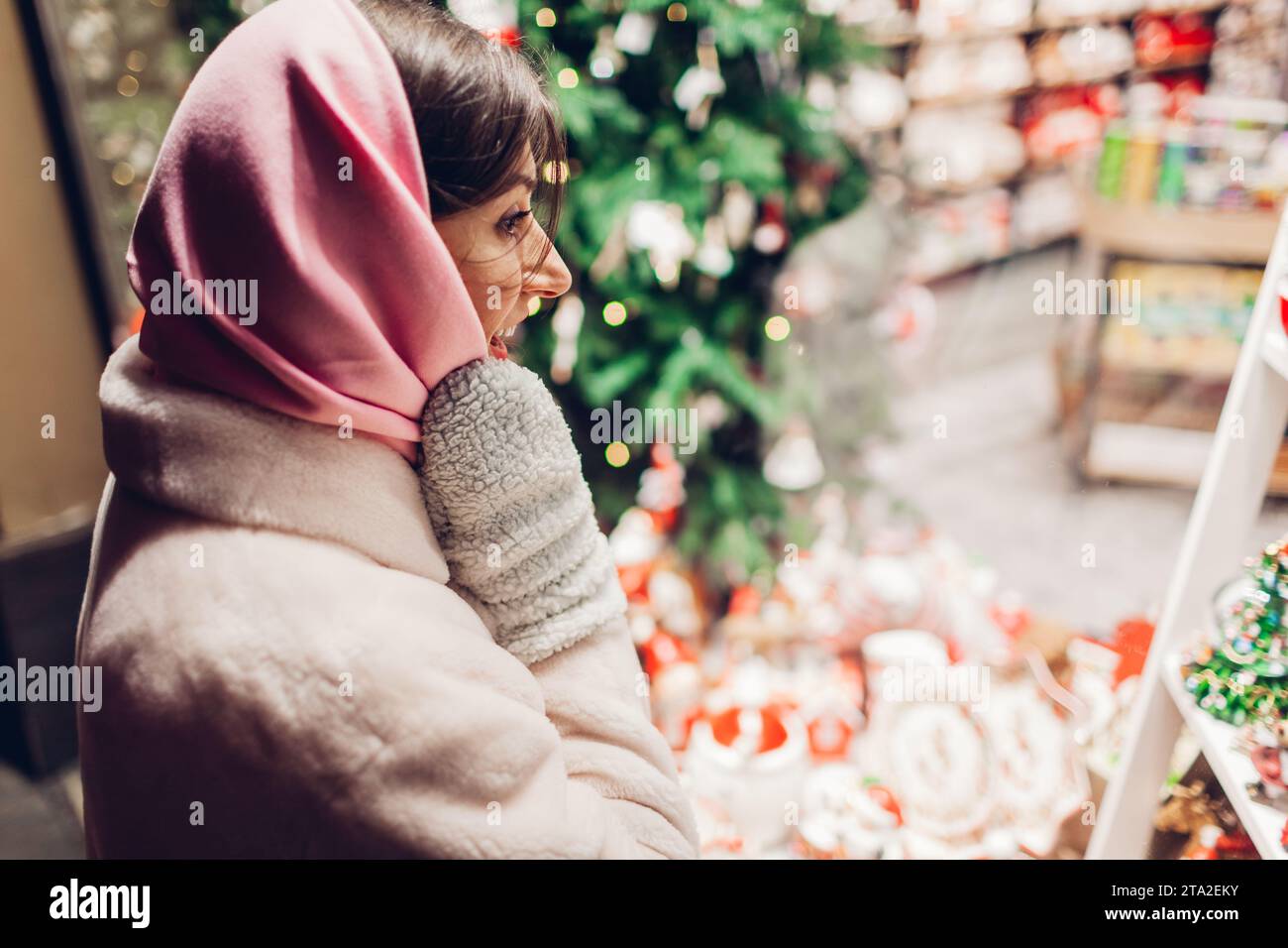 Aufgeregte Frau, die nachts auf der Straße in der Stadt Produkte auf der Weihnachtsausstellung prüft. Weihnachtseinkäufe Stockfoto