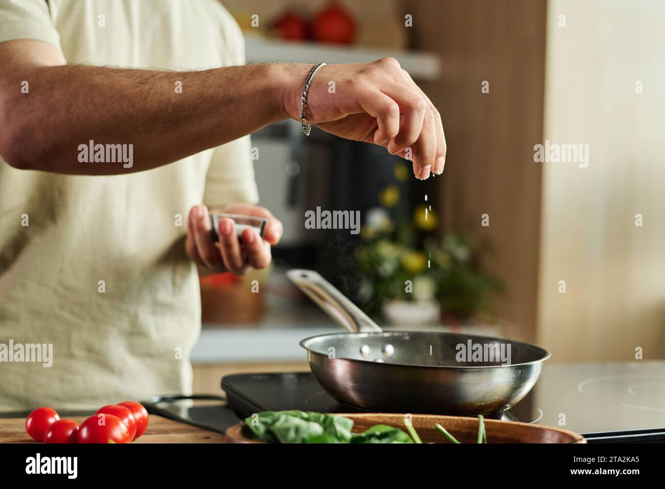 Nahaufnahme der Hände eines nicht erkennbaren Mannes, der Salz in der Pfanne auf dem Küchenherd hinzufügte Stockfoto