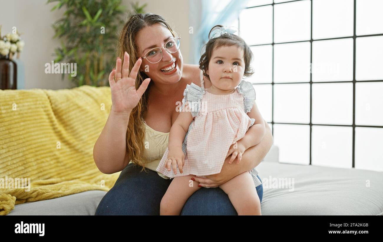 Eine reizende Mutter hält selbstbewusst die kleine Tochter in den Armen und genießt eine fröhliche, zwanglose Unterhaltung auf dem Sofa. Herzerwärmender Familienmoment voller fröhlichem Lächeln Stockfoto