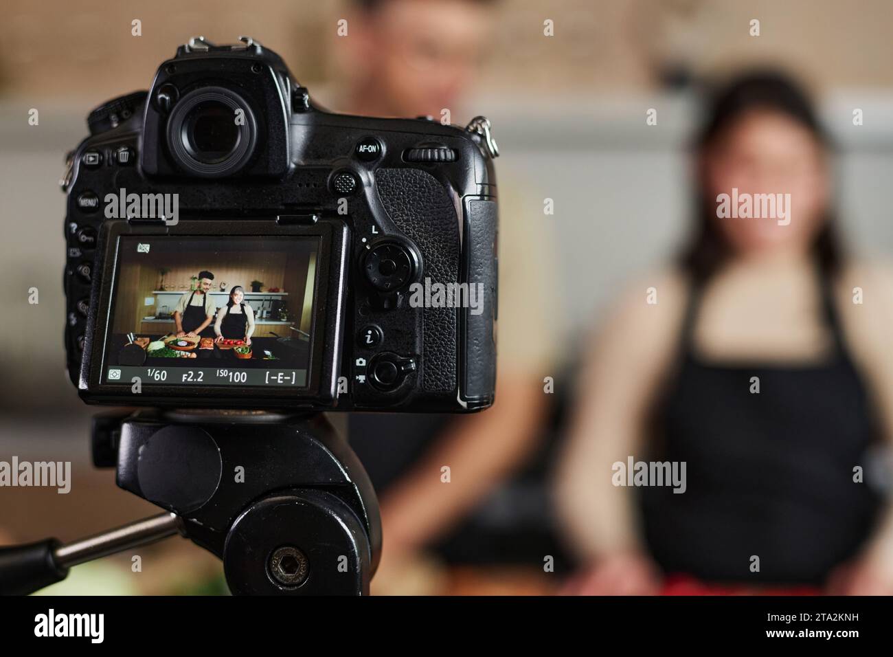 Nahaufnahme einer professionellen Digitalkamera, die Mann und Frau aufnimmt, die an der Küchentische auf dem Set der kulinarischen Show stehen, Fokus auf Kamera, Kopierraum Stockfoto