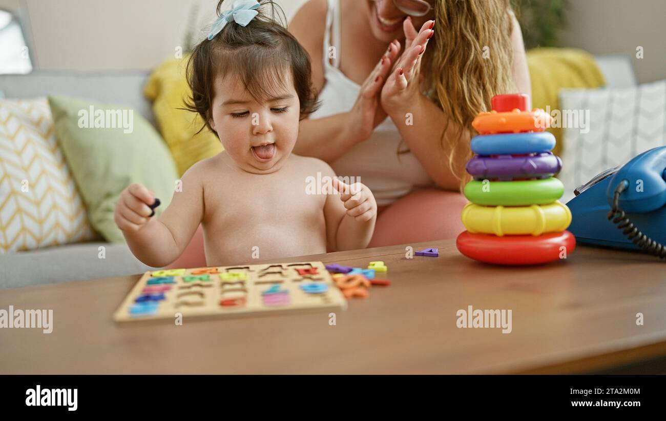 Selbstbewusste Mutter und fröhliche Tochter sitzen zusammen auf dem Sofa, spielen ein lustiges Mathematikspiel mit einem Puzzle-Spielzeug und verbreiten Positivität und Liebe in ihrem Stockfoto