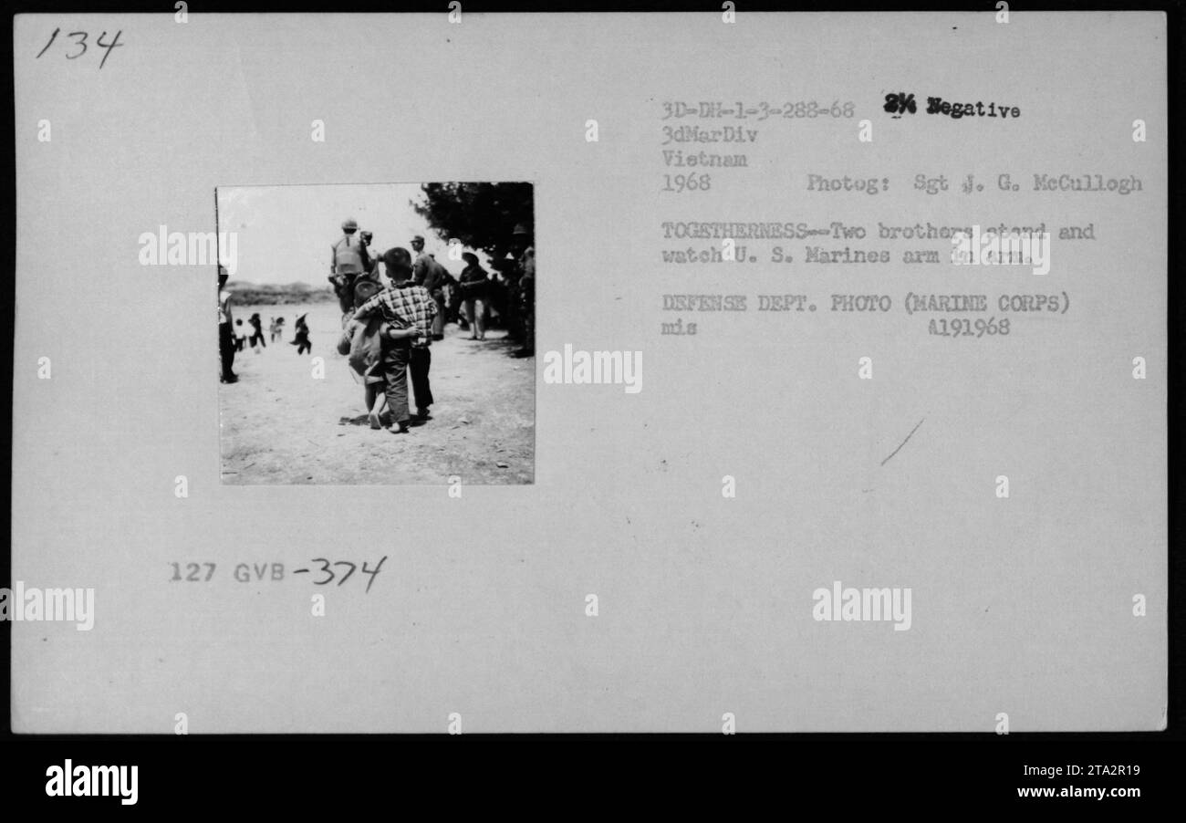 Zwei vietnamesische Brüder beobachten die US-Marines während des Vietnamkriegs in enger Verbindung. Dieses Bild zeigt die Einheit und Interaktion zwischen vietnamesischen Zivilisten und amerikanischem Militär. (Hinweis: Der in der Eingabe enthaltene Titel enthält bereits Sachinformationen und eine Beschreibung des Bildes.) Stockfoto