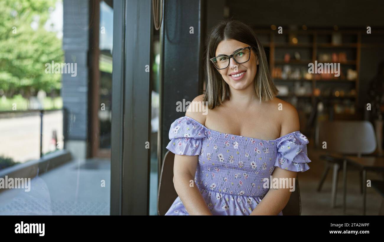 Fröhliche brünette hispanische Frau sitzt am Kaffeetisch und genießt drinnen einen Kaffee. Wunderbar lässig, sie lächelt selbstbewusst, strahlt positiv aus Stockfoto