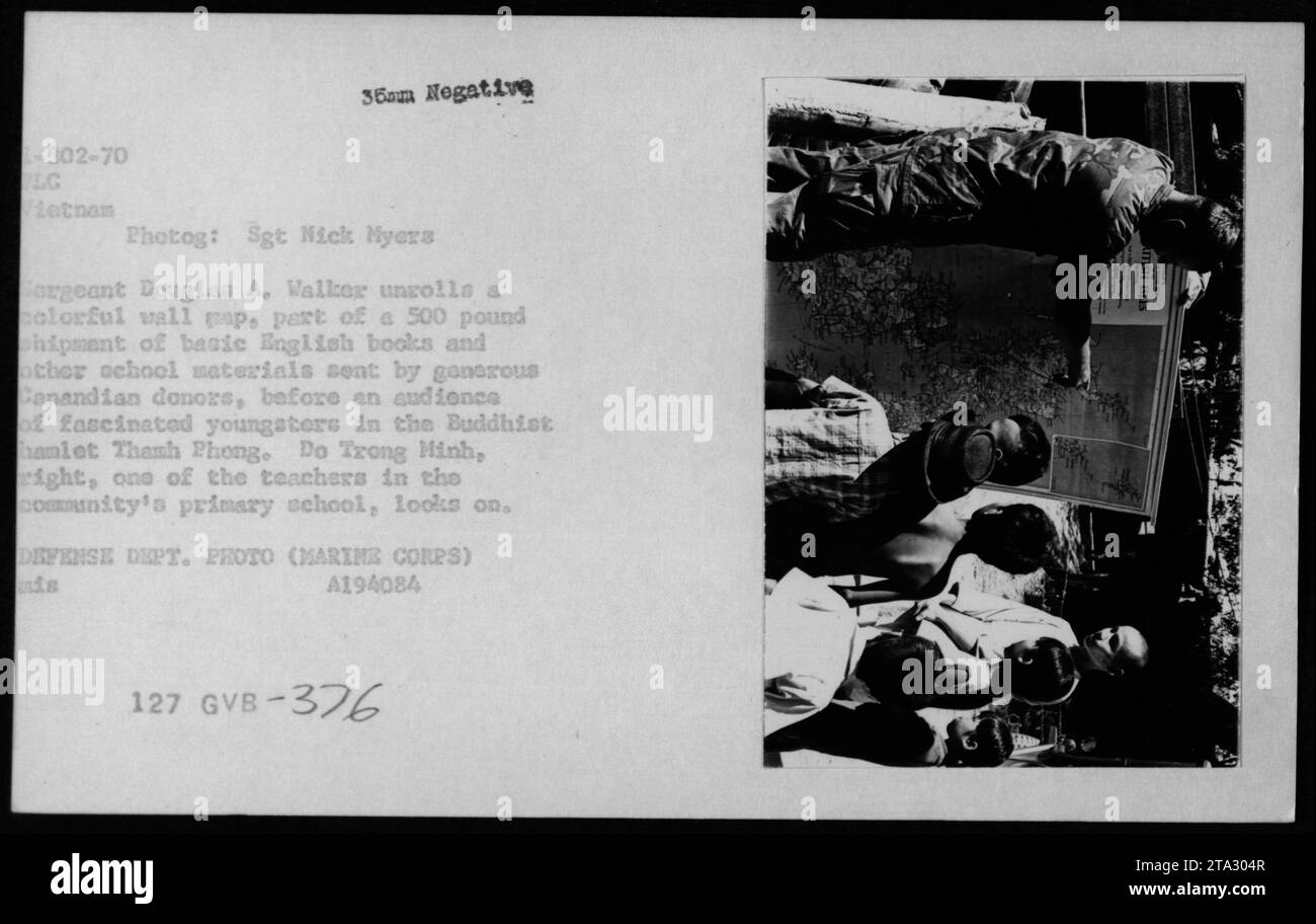 Sgt Douglas A. Walker rollt Tapeten auf und verteilt englische Bücher und Schulmaterialien, die von Kanada im buddhistischen Dorf Thanh Phong gespendet wurden, während Kinder und Lehrer Trong Minh beobachten und dabei die pädagogische Unterstützung in Vietnam 1970 hervorheben. Stockfoto