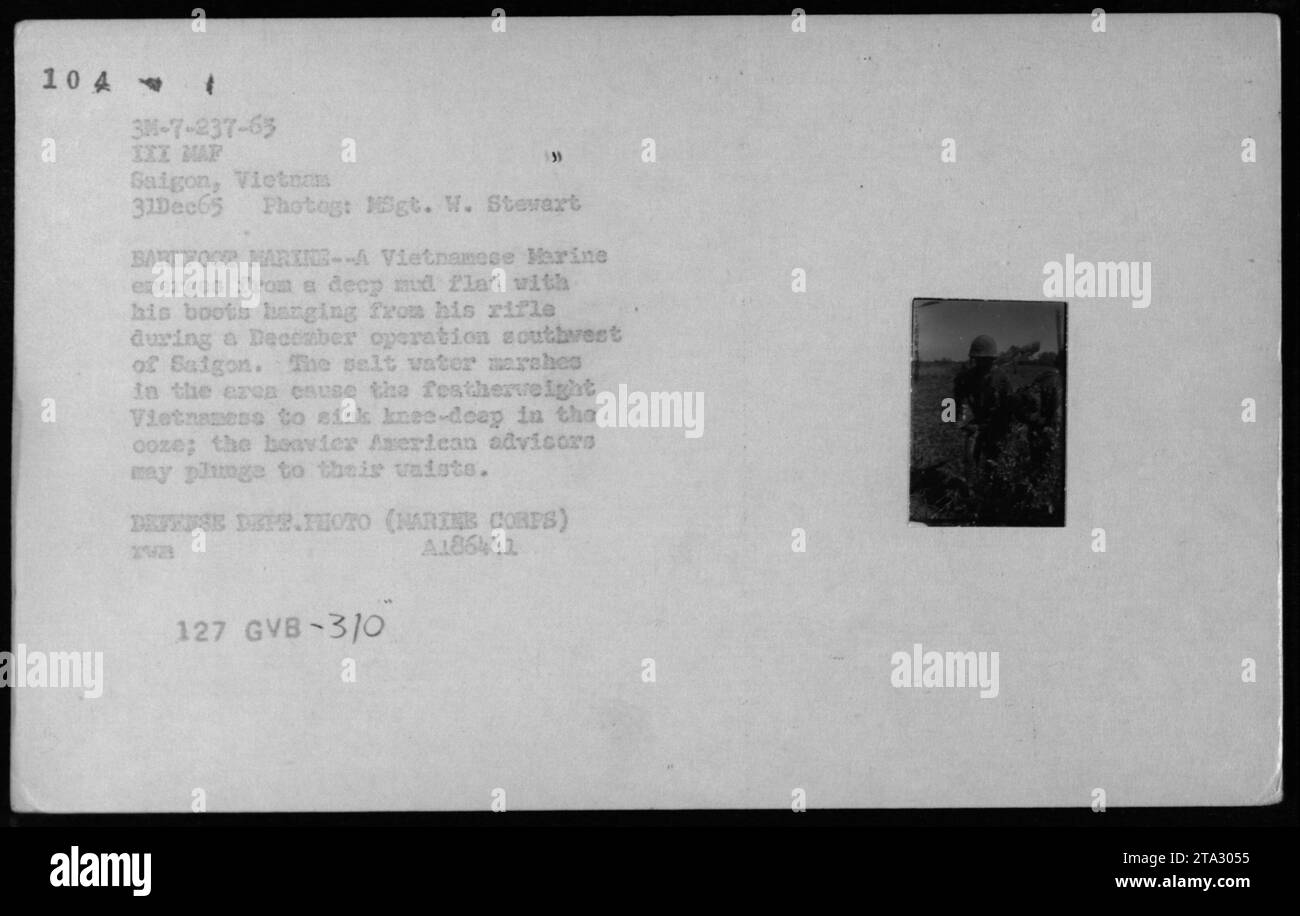 ARVN-Soldat navigiert durch ein matschiges Marschland mit seinen Stiefeln, die an seinem Gewehr hängen, während einer Dezemberoperation südwestlich von Saigon. Das sumpfige Gelände führte dazu, dass der Soldat knietief im Schlamm sank, während amerikanische Berater, die schwerere Ausrüstung trugen, das Risiko riskierten, noch weiter zu sinken. 1965. Stockfoto
