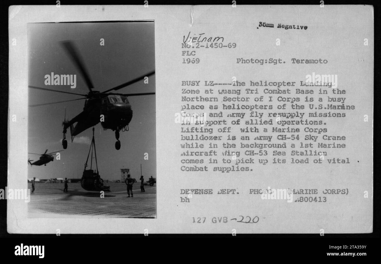 Das Bild zeigt eine belebte Hubschrauberlandezone auf der Quang Tri Combat Base im I Corps, Vietnam im Jahr 1969. Ein CH-54 Sky Crane Helikopter der Armee wird mit einem Bulldozer des Marine Corps gestartet, während im Hintergrund ein CH-53 Seehengst des 1. Marine Aircraft Wing landet, um wichtige Kampfvorräte abzuholen. Dieses Foto wurde von Sergeant Teramoto aufgenommen und ist Teil des Archivs des Verteidigungsministeriums. Stockfoto