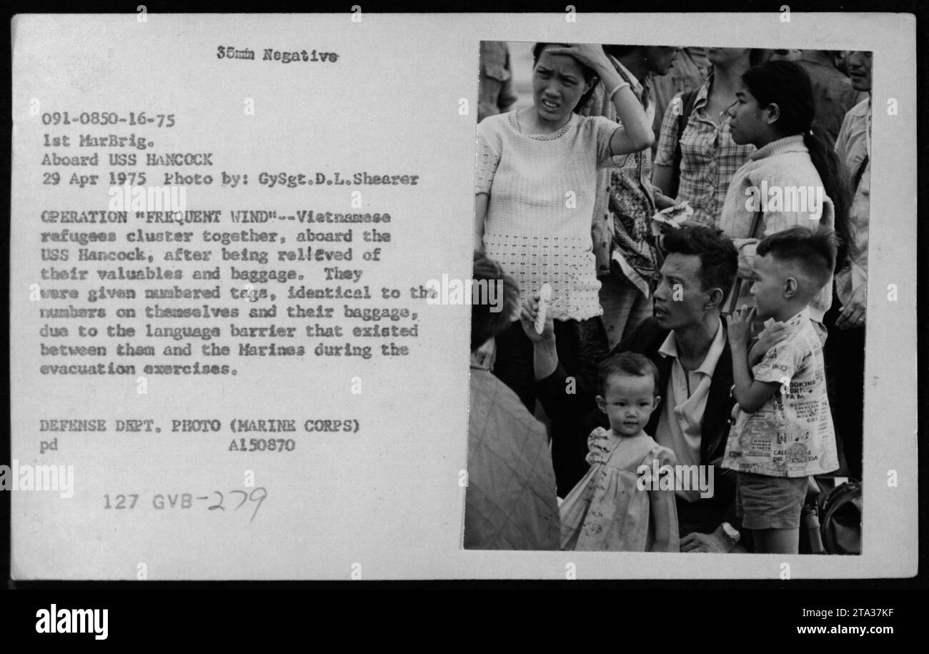 Vietnamesische Flüchtlinge an Bord der USS Hancock während der Operation Frequent Wind im Jahr 1975 sind mit nummerierten Tags zur Identifizierung geclustert, während sie Wertgegenstände und Gepäck abgeben. Stockfoto