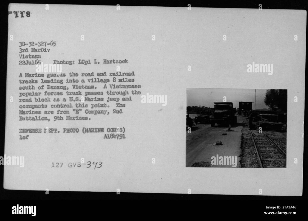 Ein Marine überwacht im Juli 1965 Straßen- und Eisenbahngleise in der Nähe von Danang, Vietnam, als ein vietnamesischer Lastwagen eine Straßensperre überquert, die von der G Kompanie, 2. Bataillon, 9. Marines, besetzt ist. Jeeps und Trucks veranschaulichen die militärische Kontrolle der Transportwege. Stockfoto
