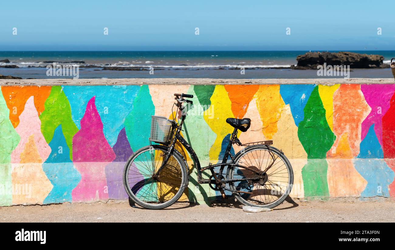 Das Fahrrad parkt an einer bunten Mauer an der Küste von Essaouira Stockfoto