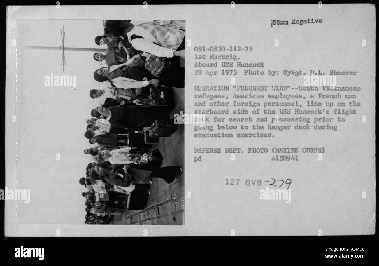 Südvietnamesische Flüchtlinge, amerikanische Mitarbeiter, eine französische Nonne und ausländisches Personal stehen am 29. April 1975 auf dem Flugdeck der USS Hancock zur Suche und Bearbeitung an, um die Operation Frequent Wind Evakuation Exercises durchzuführen. Stockfoto
