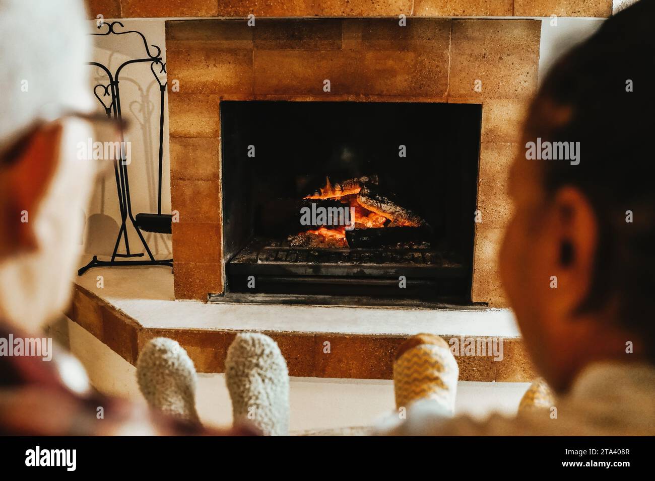 Multirassische Seniorenfreunde am Holzkamin, die sich im ländlichen Wohnzimmer aufwärmen. Winter-, Frühlings- und Urlaubsferien Stockfoto