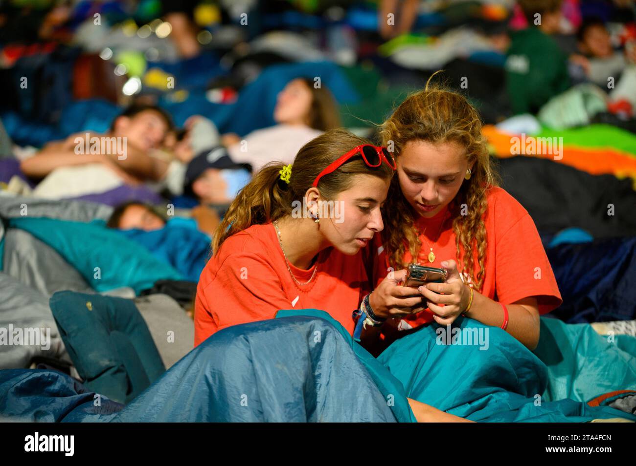 Zwei Mädchen, die vor dem Schlafen auf ein Telefon schauen. Die Mahnwache im Parque Tejo – Campo da Graca. Weltjugendtage 2023 in Lissabon, Portugal. Stockfoto