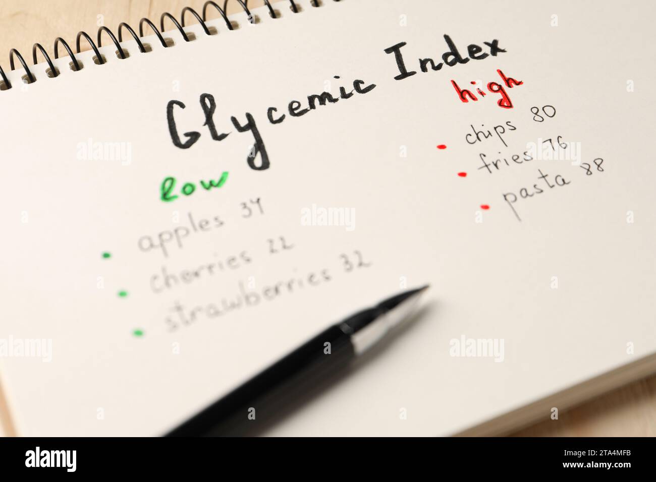 Liste mit Produkten mit niedrigem und hohem glykämischen Index in Notizbuch und Stift auf Tisch, Großansicht Stockfoto