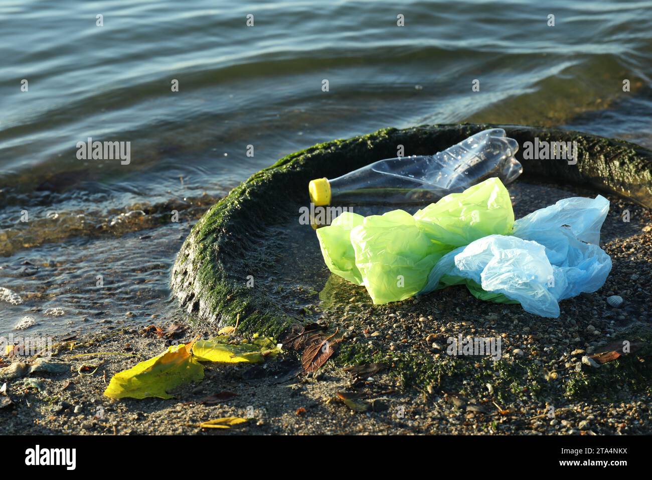 Plastikmüll und Reifen auf Sand in der Nähe von Wasser. Umweltverschmutzung Stockfoto