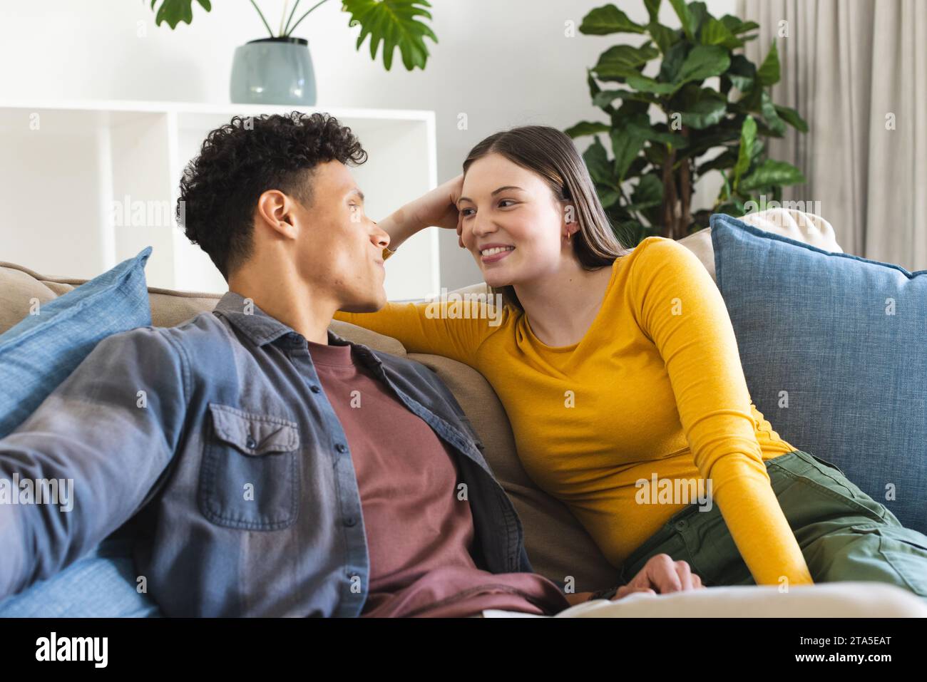 Glückliches, vielfältiges Paar, das auf der Couch sitzt und sich im Wohnzimmer zuhause ansieht, Kopierraum. Ausdruck, Liebe, Zweisamkeit und häusliches Leben u Stockfoto