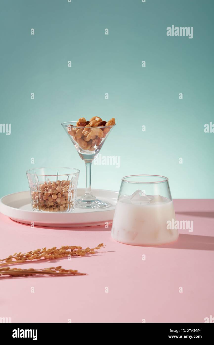 Ein kühles Glas Sojamilch mit eis, angeordnet mit rohen gemischten Nüssen und Bohnen auf rosafarbener Oberfläche. Der regelmäßige Verzehr von Nüssen kann Ihre Gesundheit in m verbessern Stockfoto
