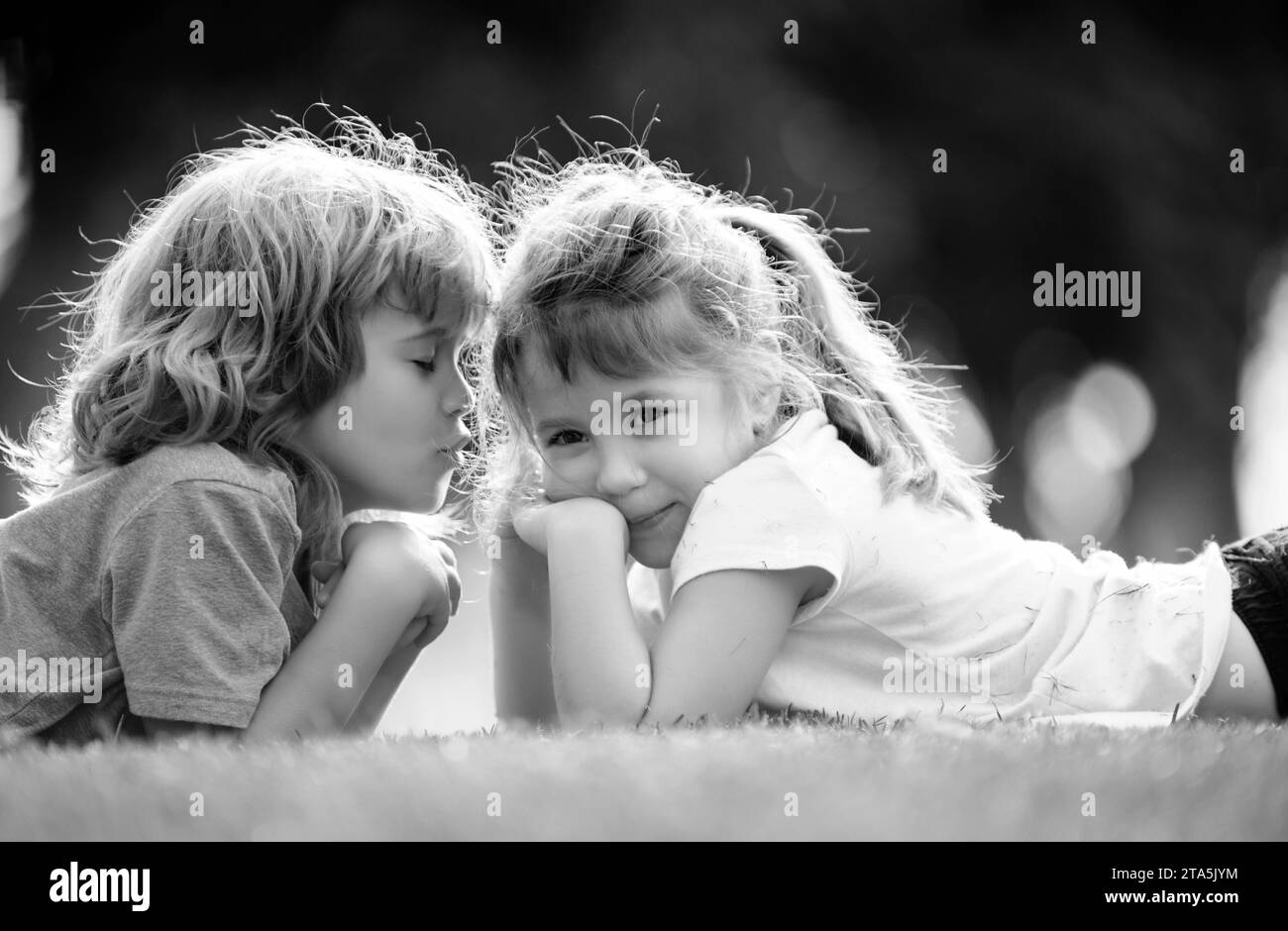 Entzückende glückliche Kinder im Freien am Sommertag, kleiner Junge küsst ein Mädchen. Schöne kleine Jungen und Mädchen, viel Spaß im Freien, auf Gras liegen. Lustige Kinder Gesicht Stockfoto
