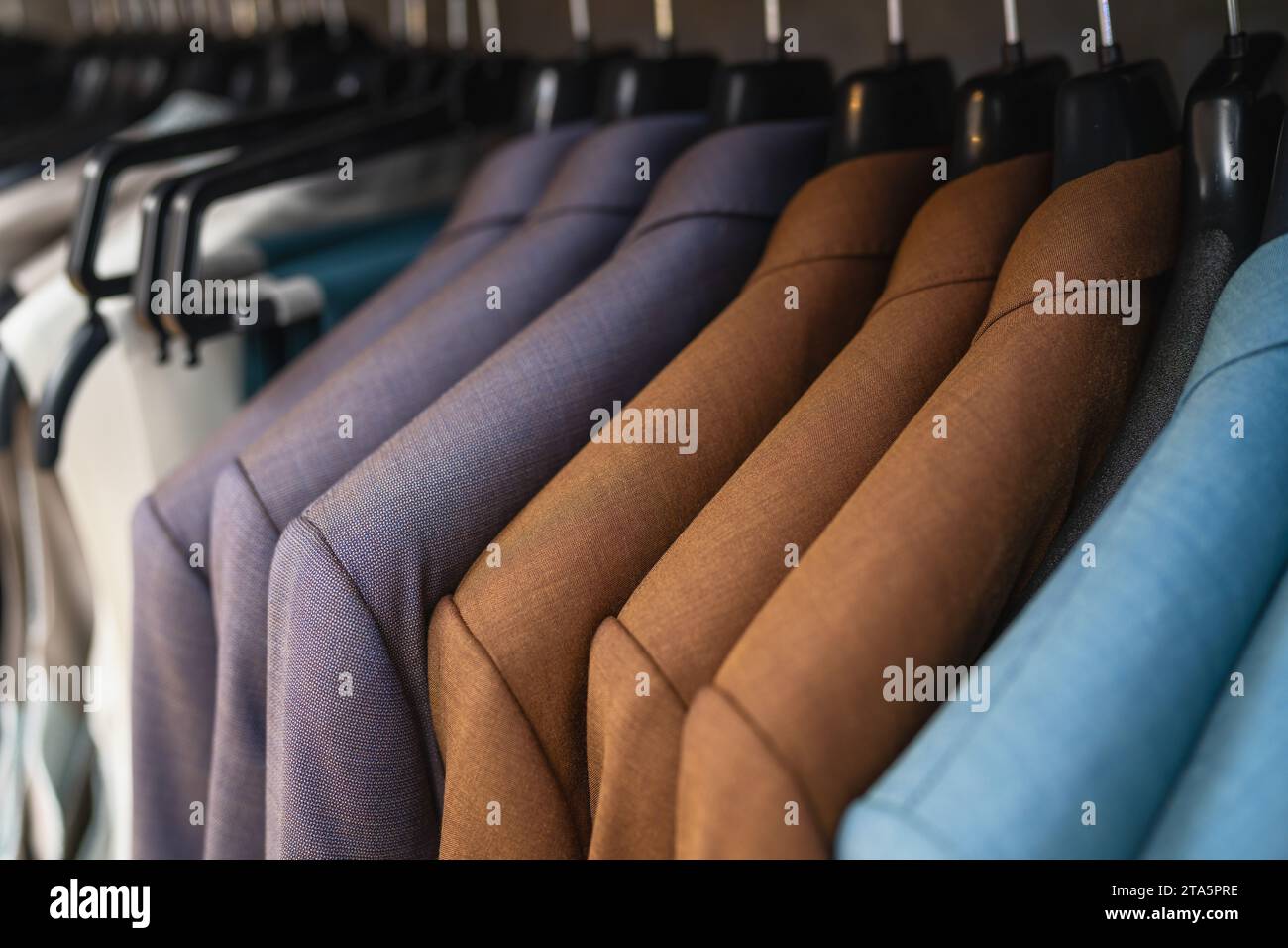Reihe von Anzügen auf Kleiderbügeln, verschiedene Braun- und Blautöne, formelle Kleidung in einem Geschäft Stockfoto