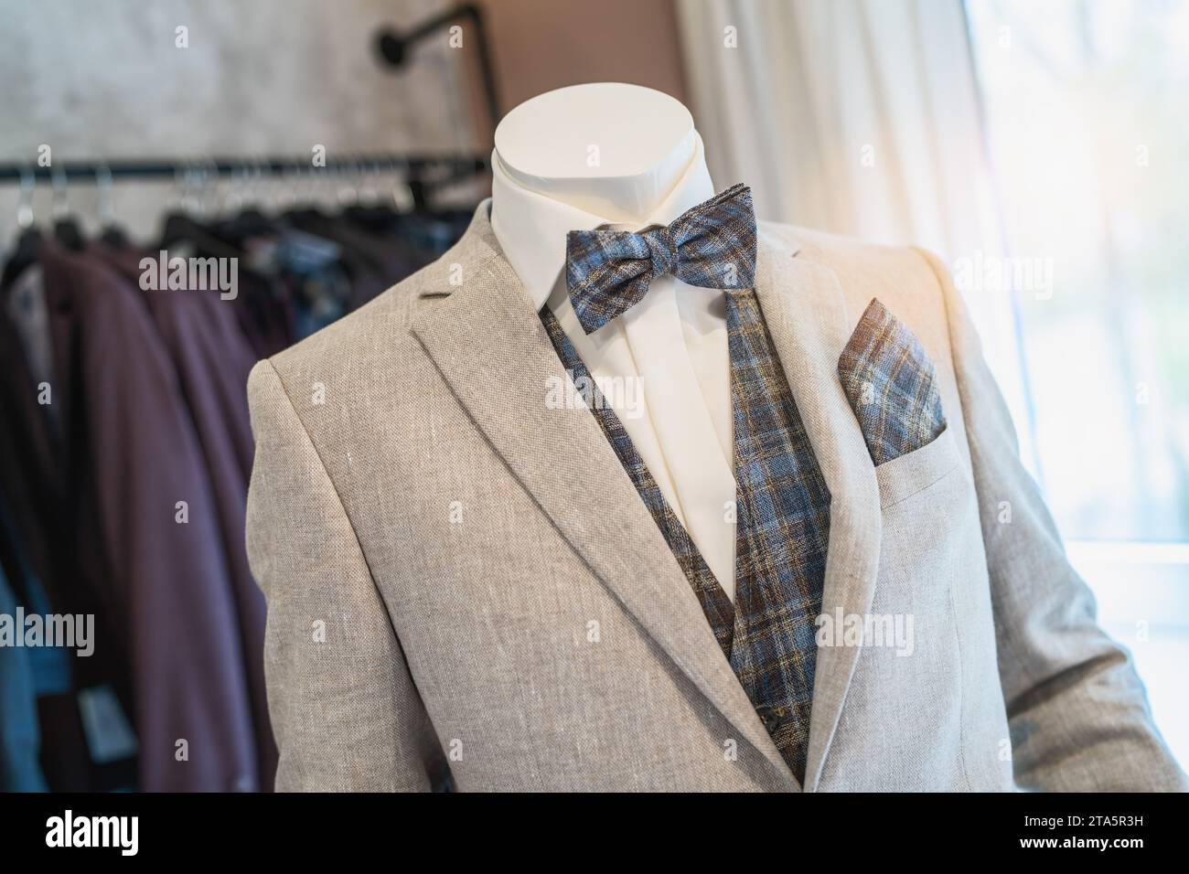 Schaufensterpuppe in einem hellgrauen Anzug mit karierter Fliege und passendem Taschenquadrat in einem Hochzeitsgeschäft Stockfoto