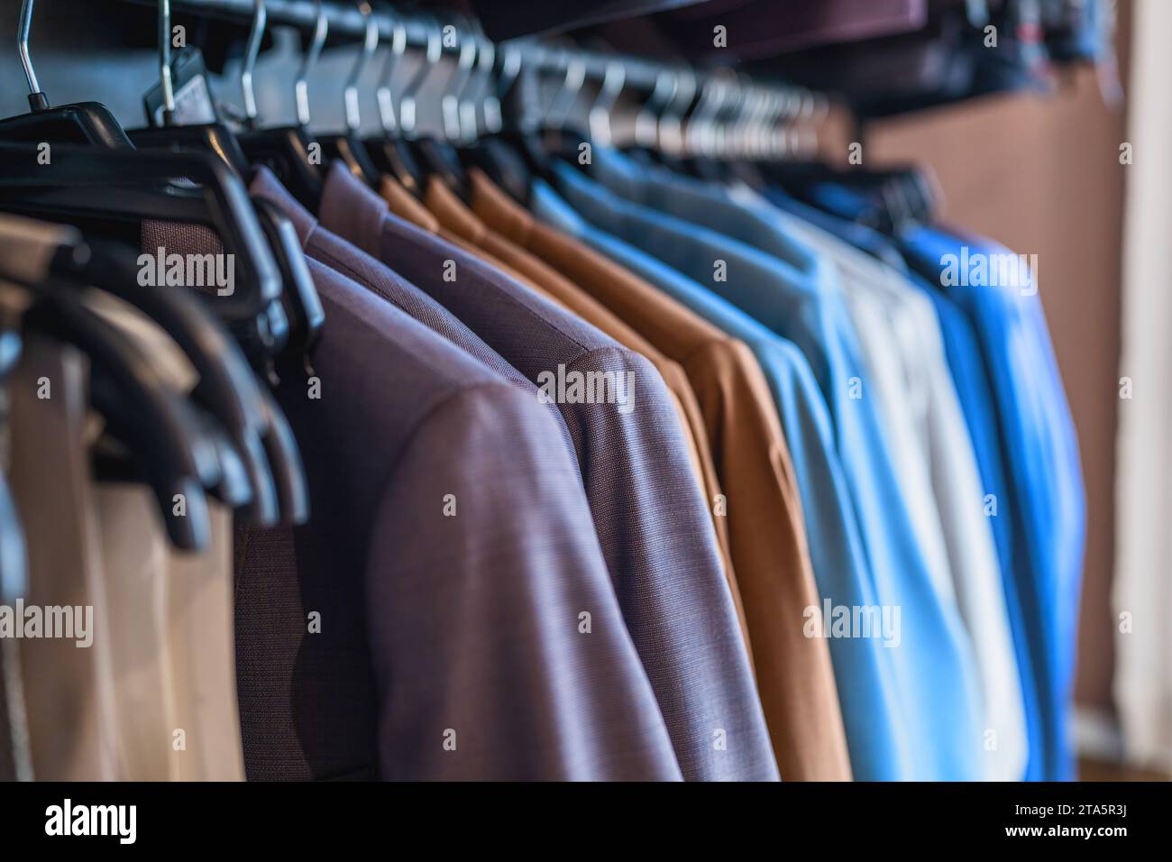 Reihe von verschiedenen farbigen Anzügen auf Kleiderbügeln in einem Bekleidungsgeschäft Stockfoto