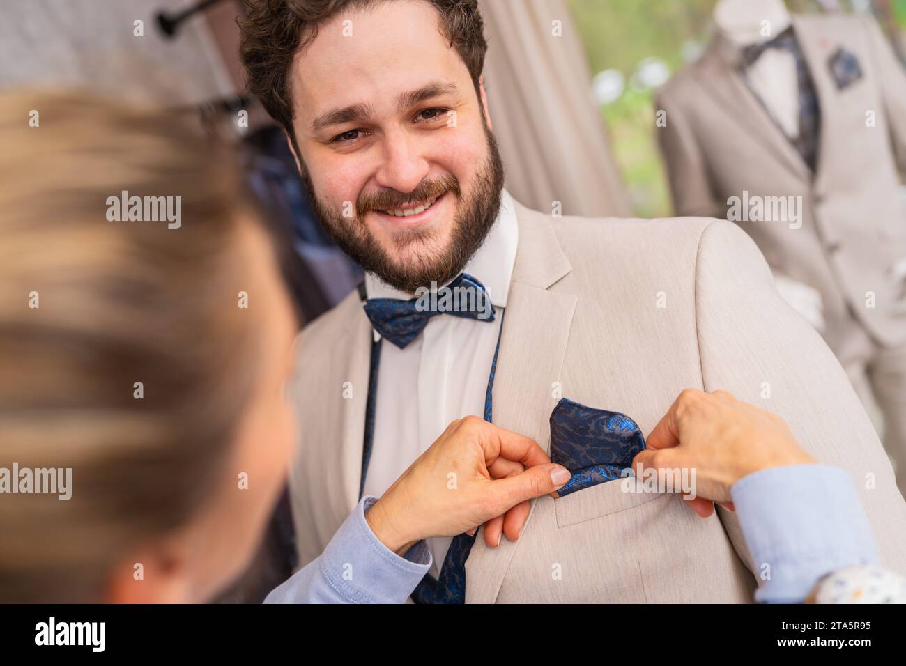 Ein Mann, der einen Anzug trägt, passt ein blaues Taschenfeld an, beide lächeln in einem Hochzeitsladen Stockfoto