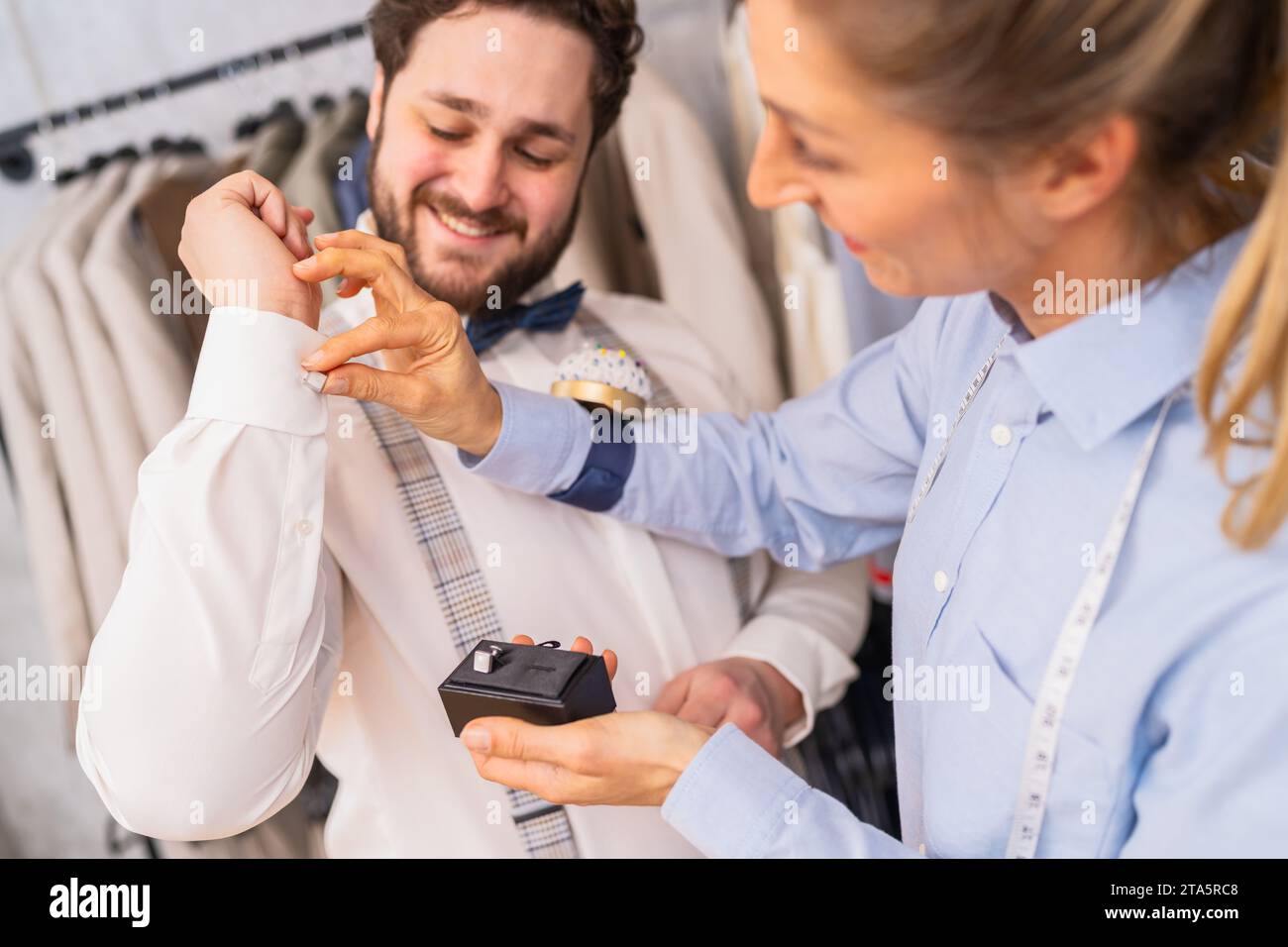 Schneider hilft einem Mann mit Manschettenknöpfen, beide teilen einen freudigen Moment Stockfoto