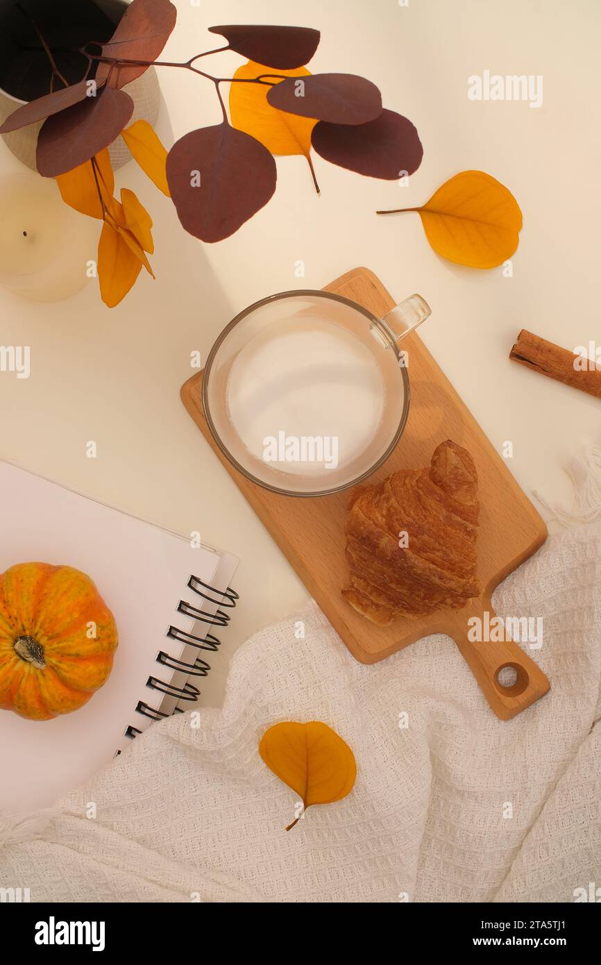 Auf einem hellbeigen Hintergrund, der mit bunten getrockneten Blättern verziert ist, wird ein Holztablett mit Kuchen und Kaffeetassen ausgestellt. Draufsicht, professionell Stockfoto