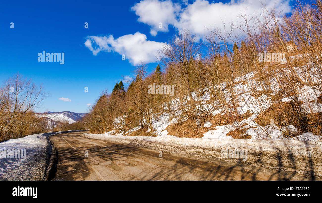 Alte Straße führt durch schneebedeckte Hügel. Bergige Winterlandschaft an einem sonnigen Tag unter blauem Himmel mit Wolken Stockfoto