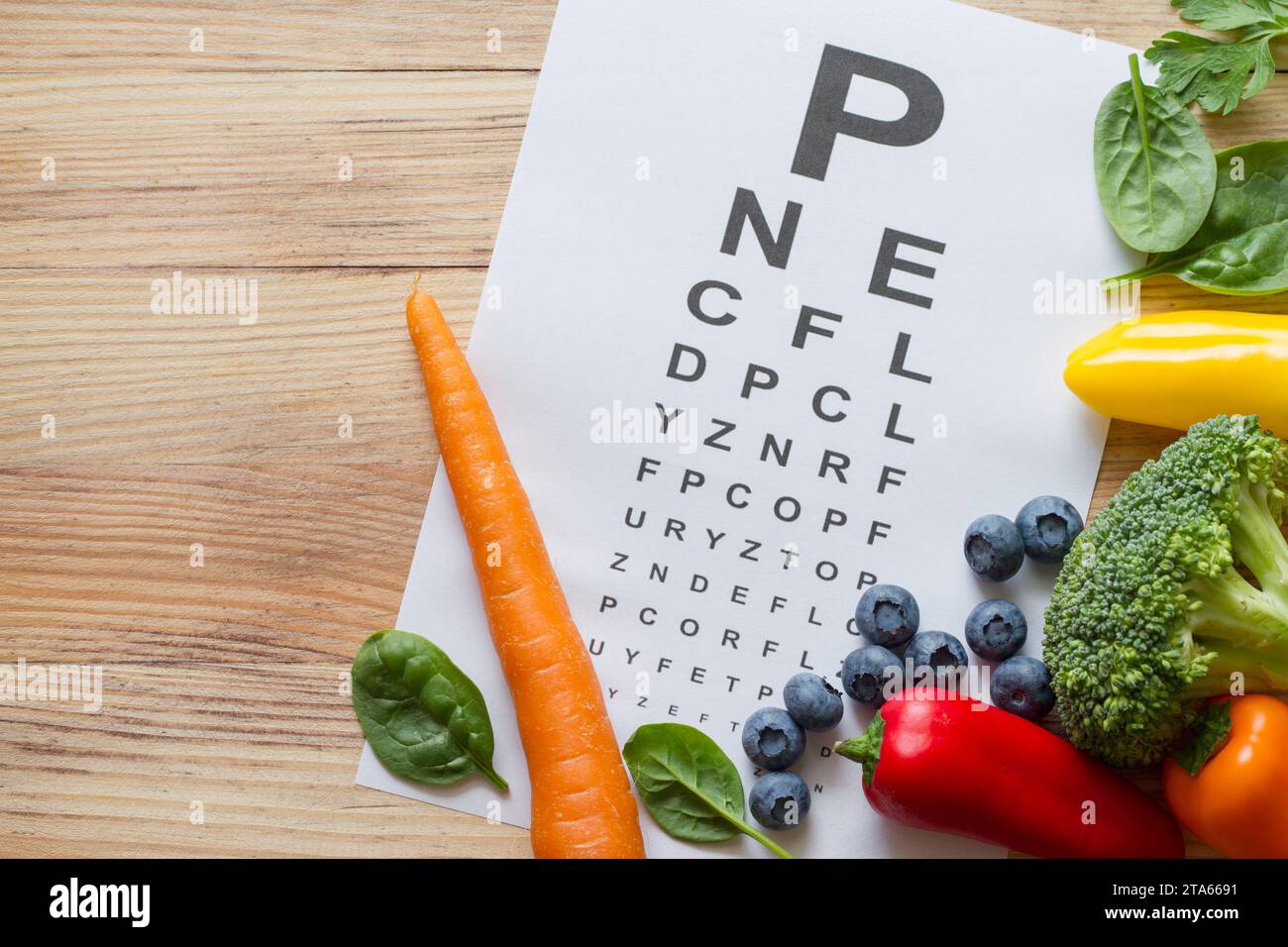 Nahrung für Augen Gesundheit, buntes Gemüse und Früchte, reich an Lutein und Auge Test Diagramm auf hölzernem Hintergrund, Konzept Stockfoto