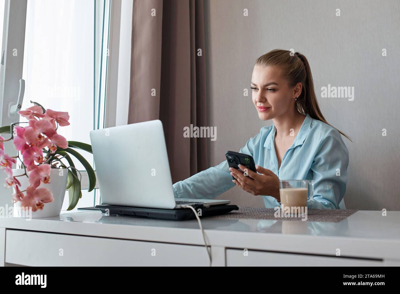 Eine junge Frau, die einen Laptop benutzt, kommuniziert über das Internet mit einem Kunden aus dem Wohnzimmer. Gemütlicher Arbeitsplatz, Fernarbeit, E-Learning-Konzept Stockfoto