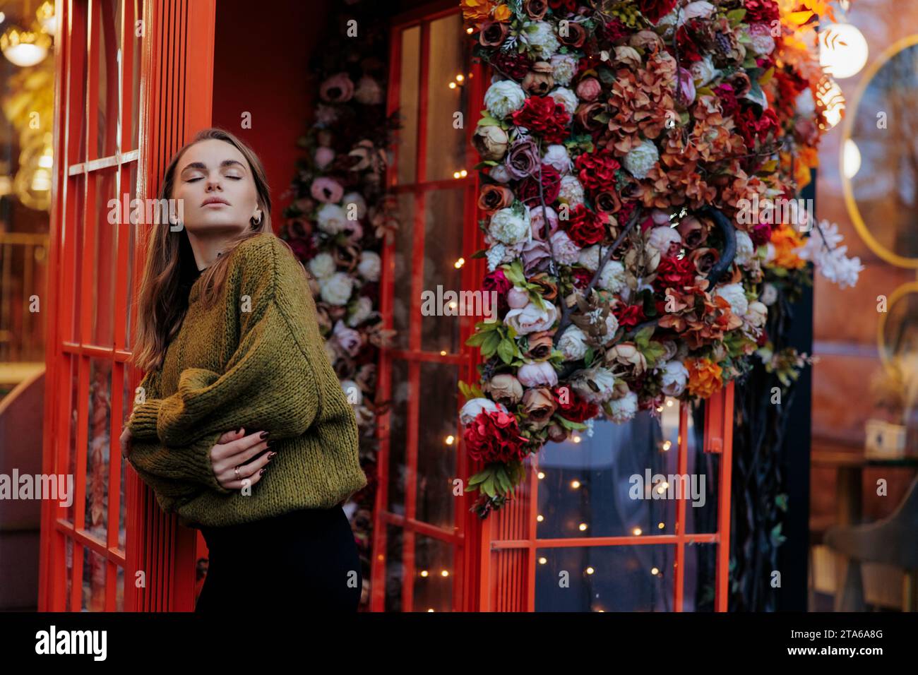 Blick auf die junge traurige Frau, die in der Nähe steht und mit Blumengirlanden und Lichtern geschmückt ist. Nahaufnahme. Stockfoto