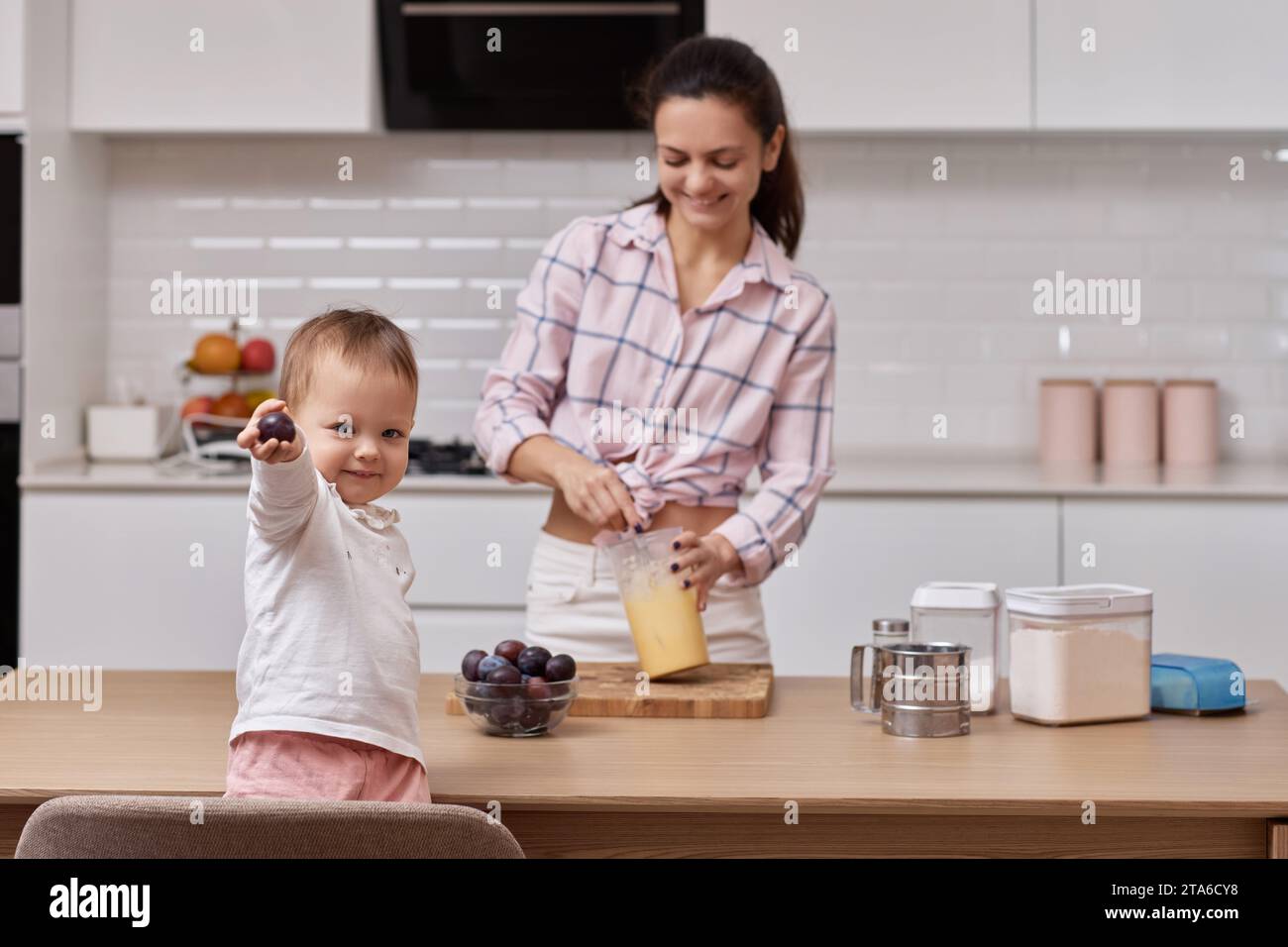 Mutter mit ihrer kleinen Tochter bereitet Pflaumenkuchen in der Küche vor. Zusammen backen Stockfoto