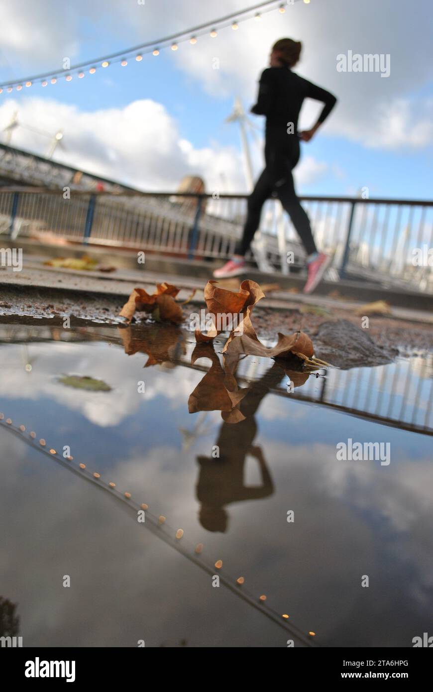 Ein Jogger läuft an einer herbstlichen Pfütze in Londons Southbank vorbei. Stockfoto