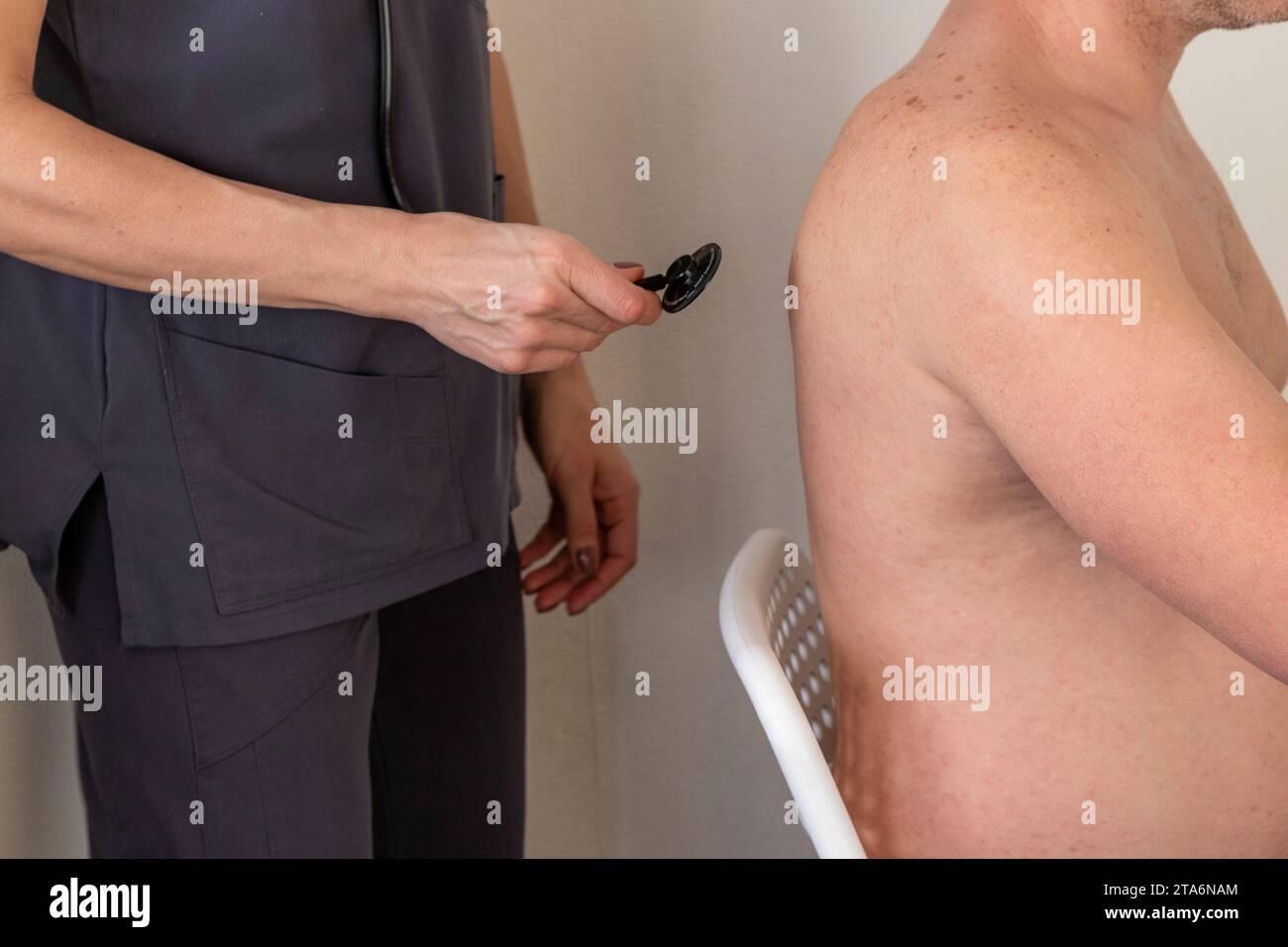 Schuss der Ärztin in Uniform gegen die weiße Wand, die den mitteljährigen männlichen Patienten untersucht Stockfoto