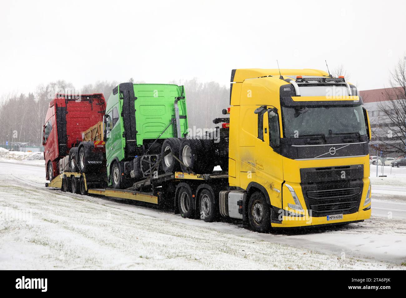 Gelber Volvo FH-Lkw mit zwei neuen grünen und roten Volvo-Lkw, die bei Winterschnee geparkt sind. Salo, Finnland. November 2023. Stockfoto