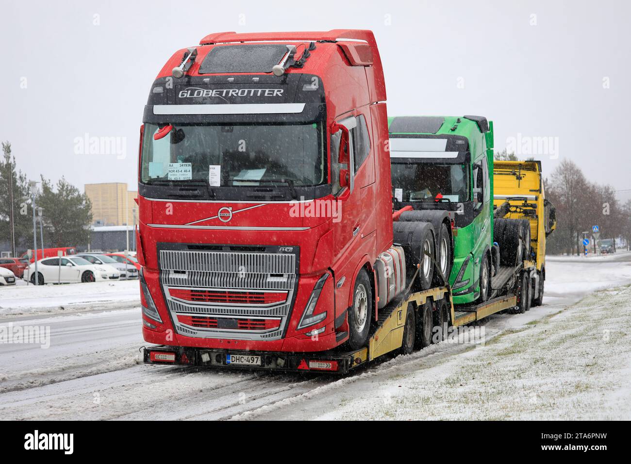 Neues, rotes Volvo FH16 Truck Globetrotter Fahrerhaus und grüner Volvo Truck im Winter auf Volvo Fahrzeugträger LKW geladen. Salo, Finnland. November 2023. Stockfoto
