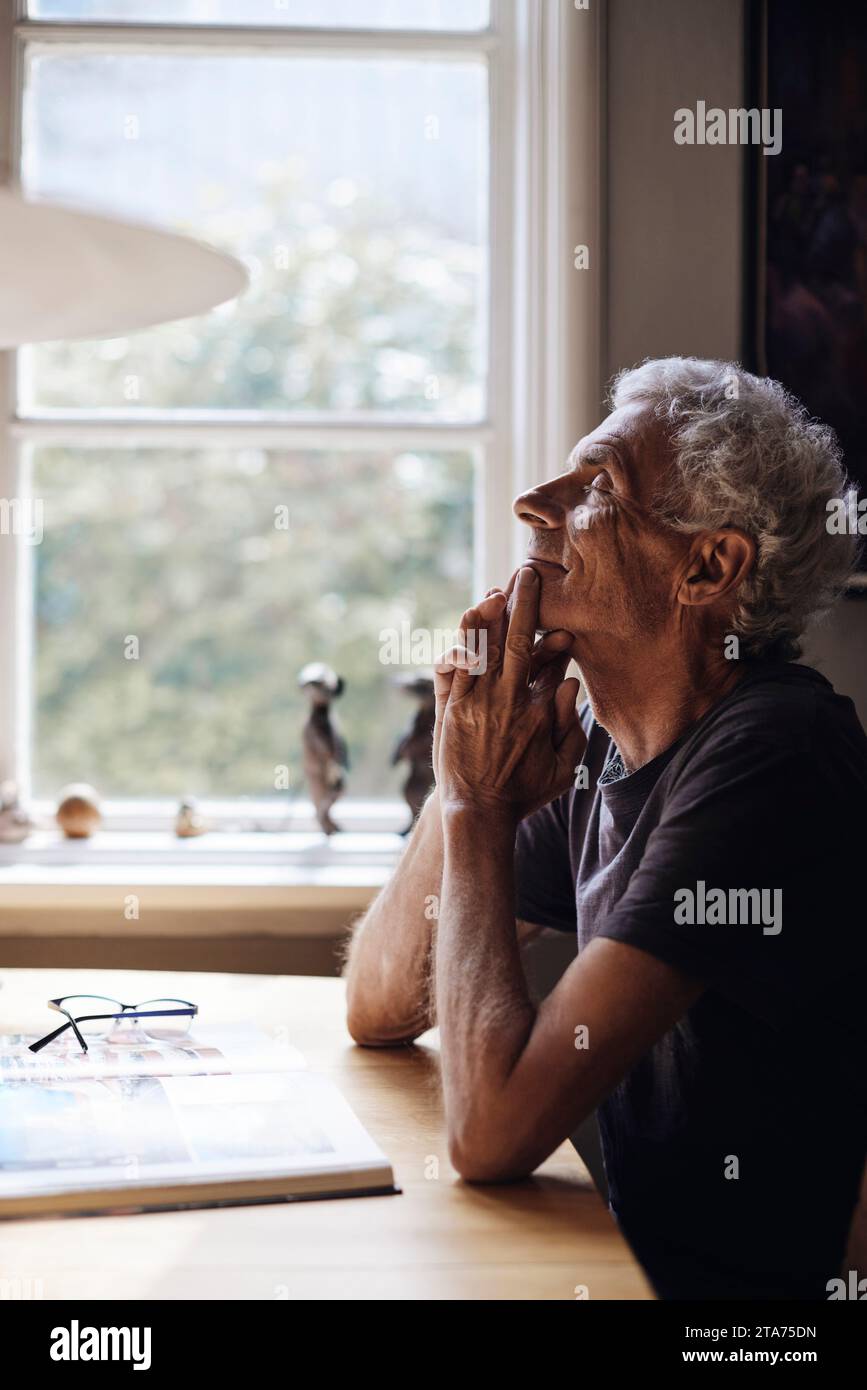 Seniorenmann mit geschlossenen Augen, der zu Hause auf dem Tisch träumt Stockfoto