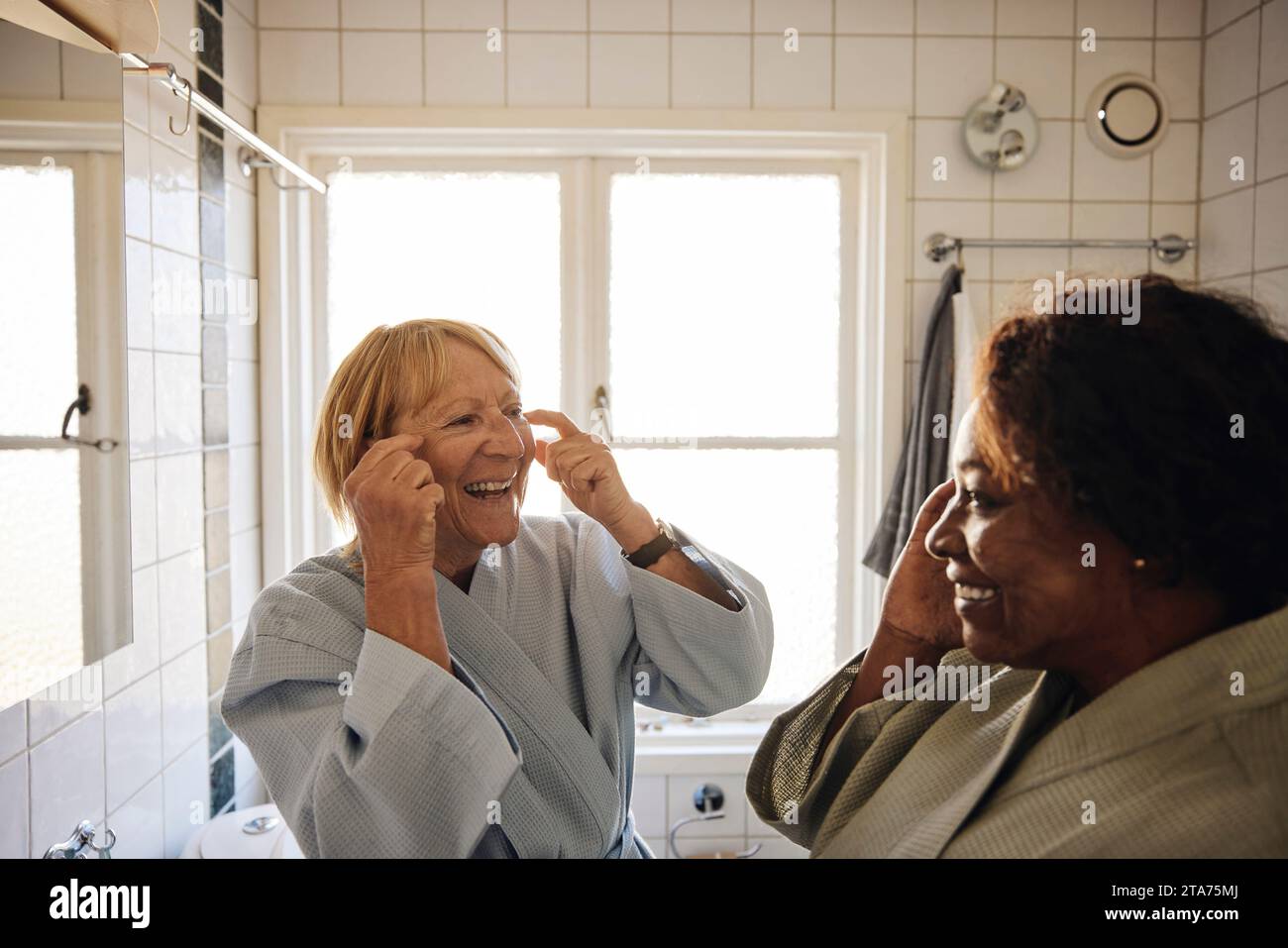 Glückliche multirassische Freundinnen, die Hautpflege zusammen im Badezimmer zu Hause machen Stockfoto