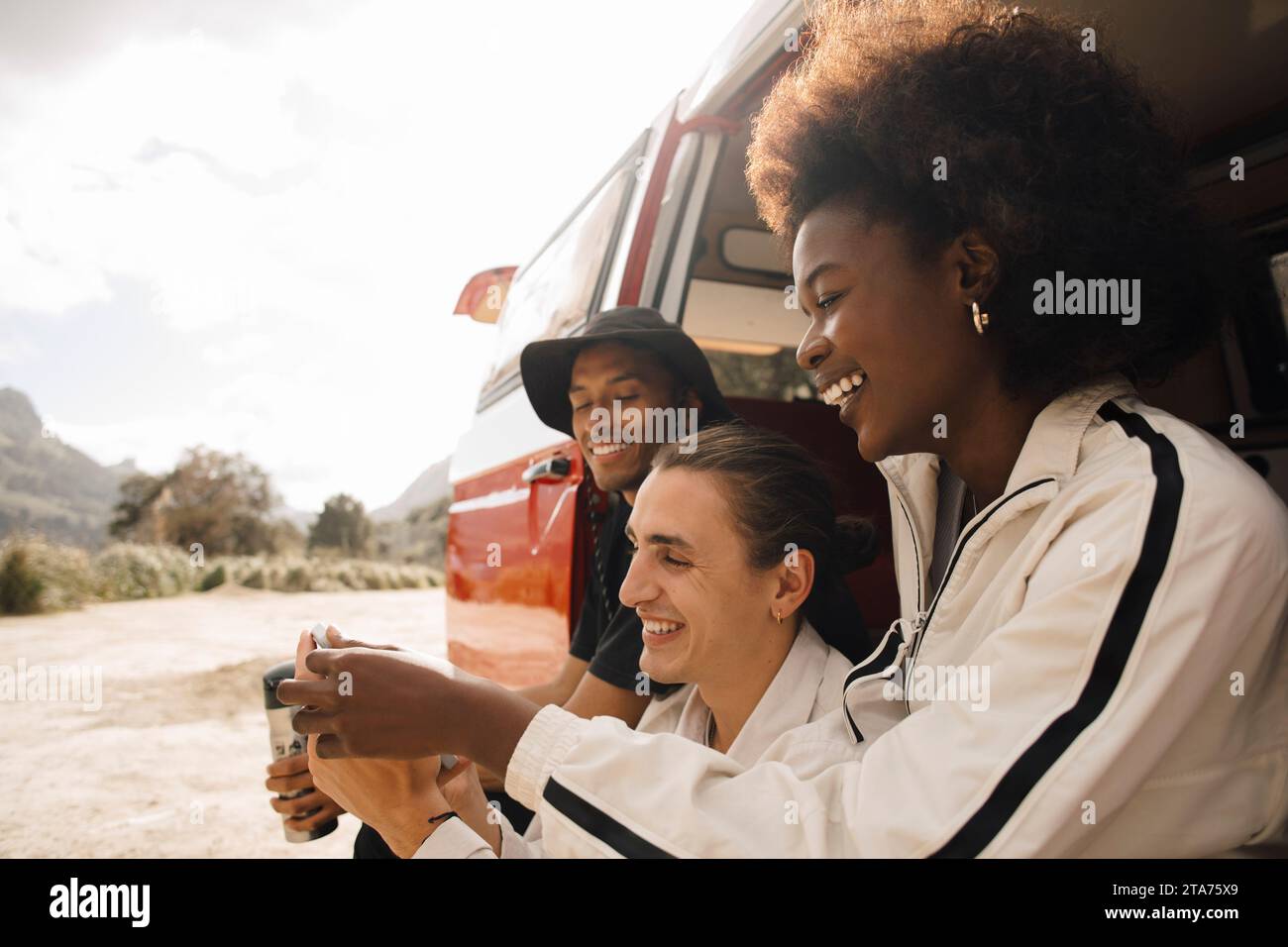 Glückliche, männliche und weibliche, multirassische Freunde, die ihr Smartphone teilen, während sie im Van sitzen Stockfoto